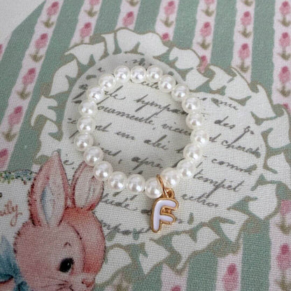 Initial Pearl Necklace with faux pearls and gold letter charm on floral background, elegant accessory.