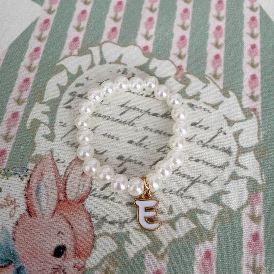 Initial Pearl Necklace with faux pearls and an elegant 'E' charm, resting on vintage floral fabric.