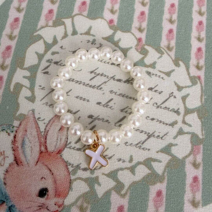 Initial Pearl Necklace with faux pearls and a delicate letter charm, resting on floral patterned fabric.