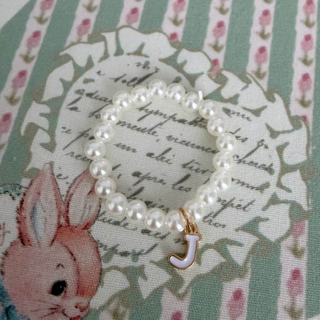 Initial Pearl Necklace with faux pearls and a delicate letter 'J' charm on a floral background.