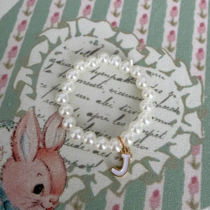Initial Pearl Necklace with faux pearls and a delicate letter 'J' charm on a floral background.