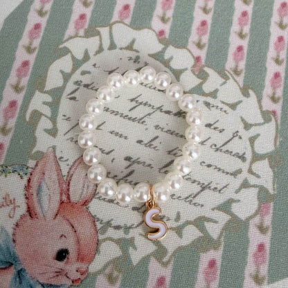 Initial Pearl Necklace with faux pearls and a delicate letter charm on a patterned background.