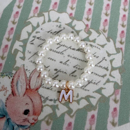 Initial Pearl Necklace with faux pearls and gold letter charm on floral fabric background.