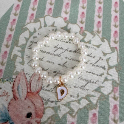 Initial Pearl Necklace with faux pearls and a delicate 'D' charm, set on a floral patterned background.