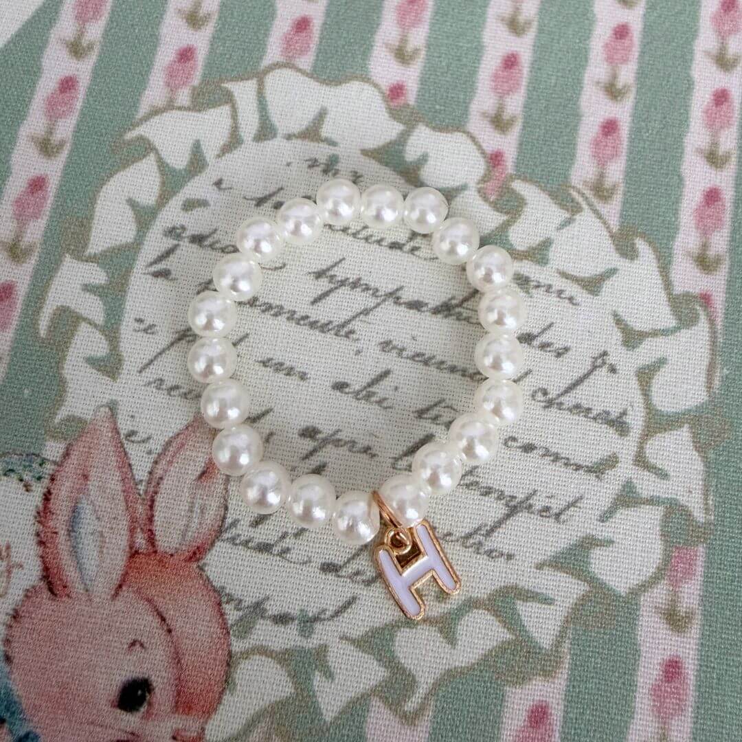 Initial Pearl Necklace featuring faux pearls and a delicate letter 'H' charm on a vintage floral fabric background.