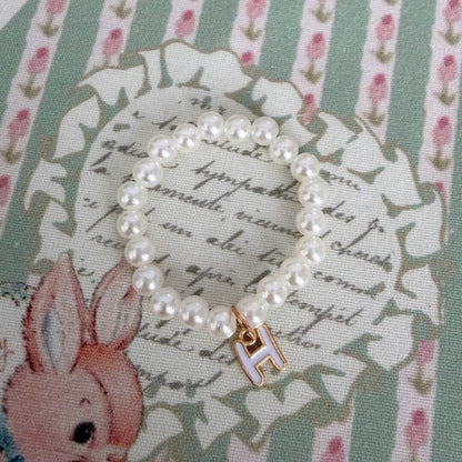 Initial Pearl Necklace featuring faux pearls and a delicate letter 'H' charm on a vintage floral fabric background.