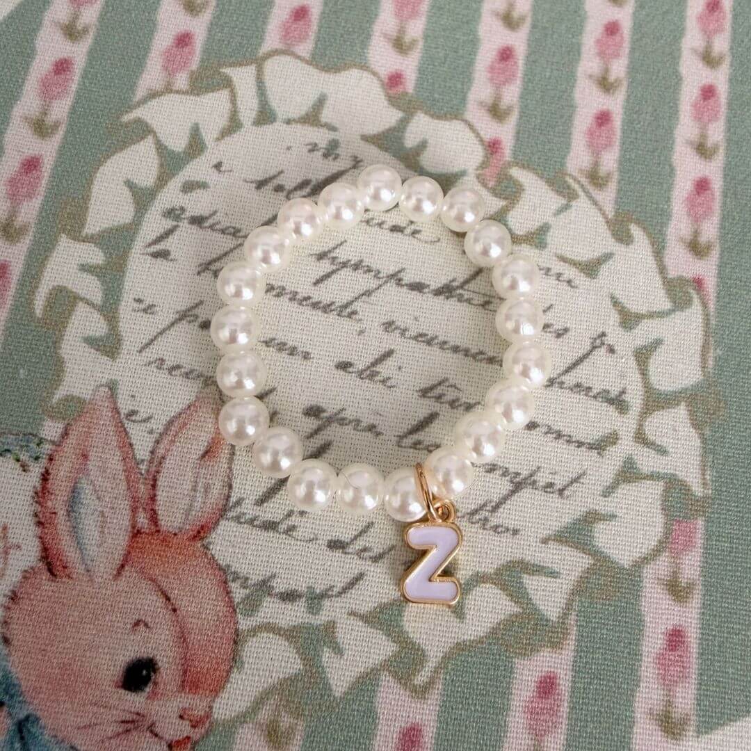 Initial Pearl Necklace with soft faux pearls and a gold letter charm on a floral patterned background.