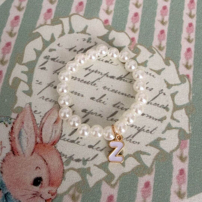 Initial Pearl Necklace with soft faux pearls and a gold letter charm on a floral patterned background.
