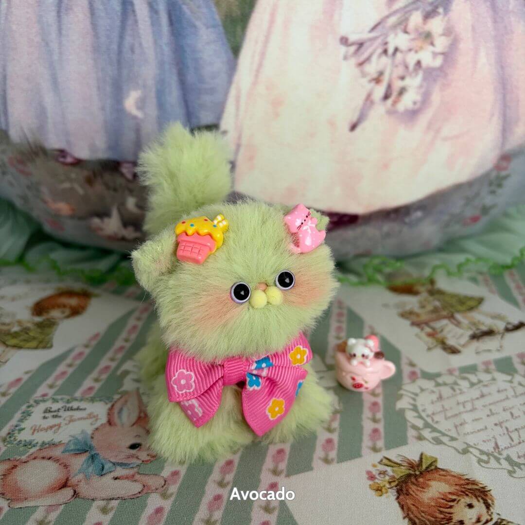 Handmade kitten figurine in soft avocado green, wearing a pink bow and cupcake hat, part of the Fruity Kitten Collection.