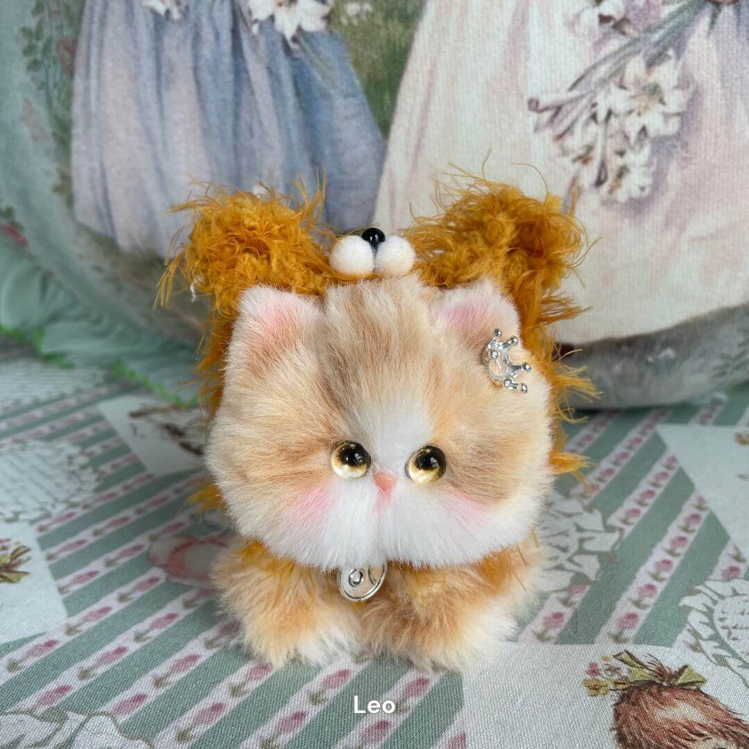 Leo-inspired handmade kitten plush toy with crown accessory from the Zodiac Kitten Collection on decorative background.