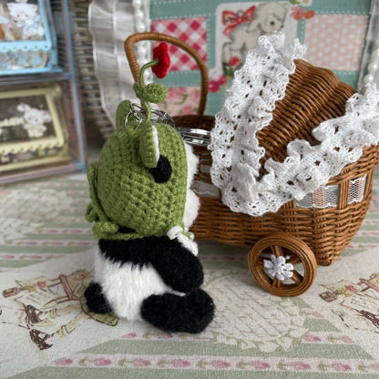 Handmade mini panda plush with green hat and apron, displaying movable joints, beside a decorated wicker basket on a vintage cloth.