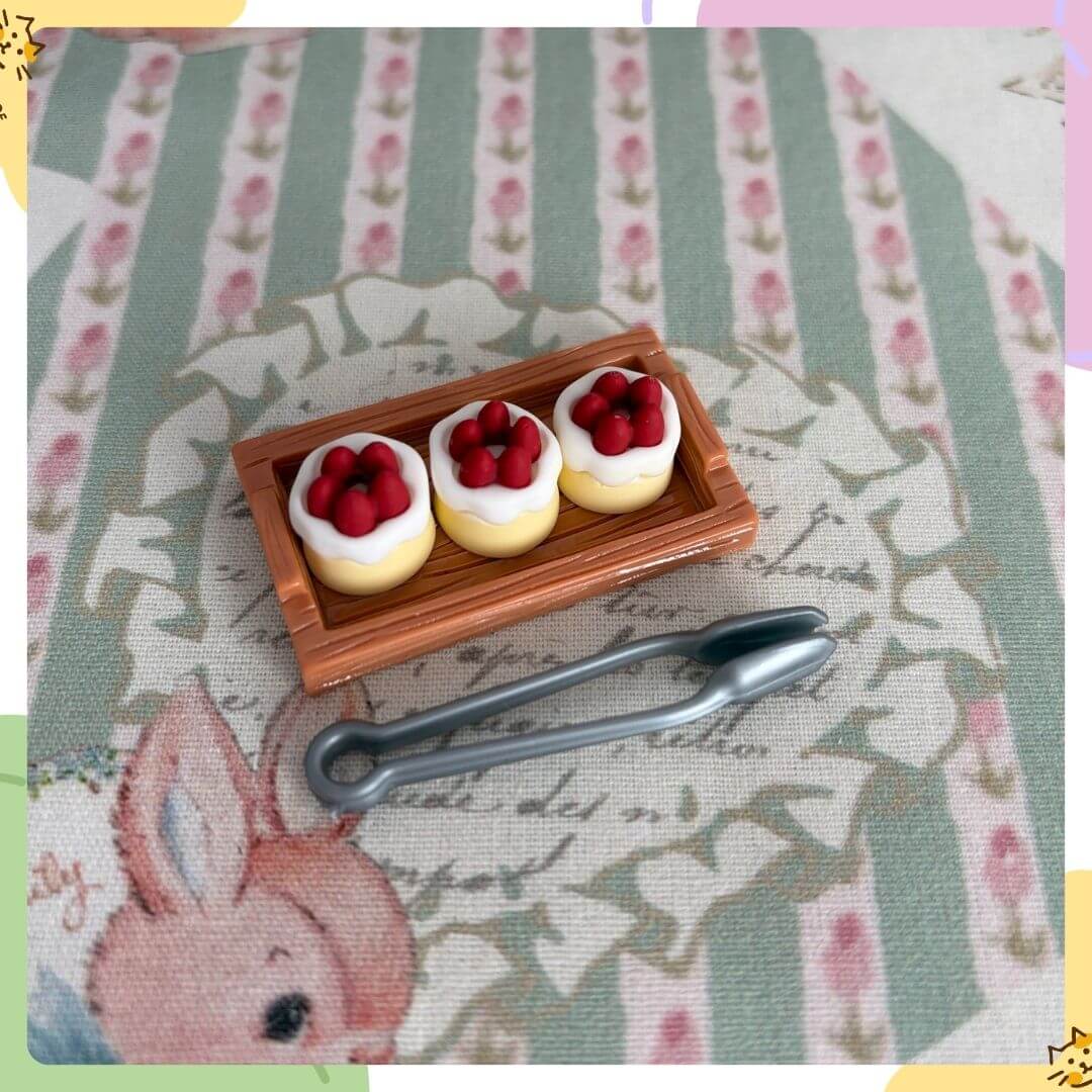 Mini Strawberry Cake Set featuring three cute cakes topped with strawberries, accompanied by a silver serving tool on whimsical fabric.