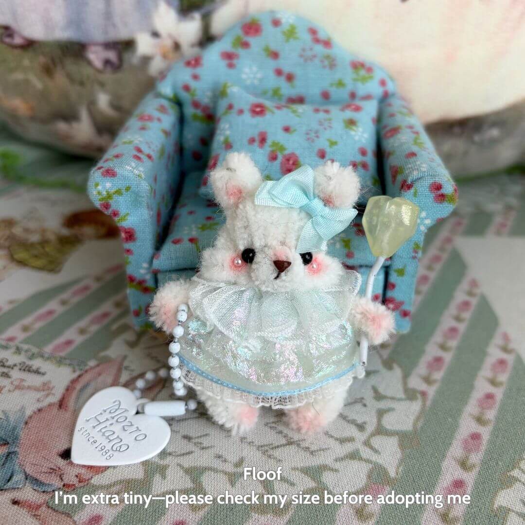 Miniature Pipe Cleaner Animals: handmade fluffy kitten figurine in pastel dress with bow, seated beside floral chair.
