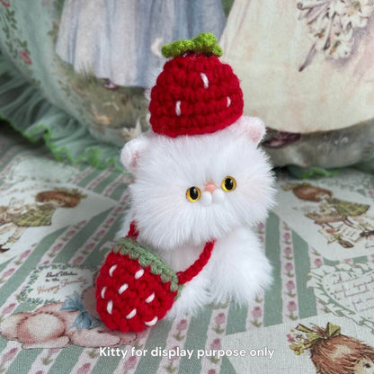 Fluffy white plush cat wearing a red strawberry hat and bag, sitting on a floral fabric backdrop. Perfect accessory for plush toys.