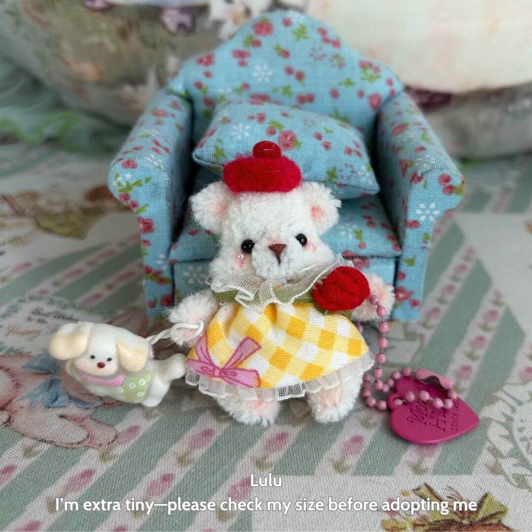 Adorable miniature pipe cleaner bear in yellow dress and red hat, next to a tiny dog, sitting on a floral chair.