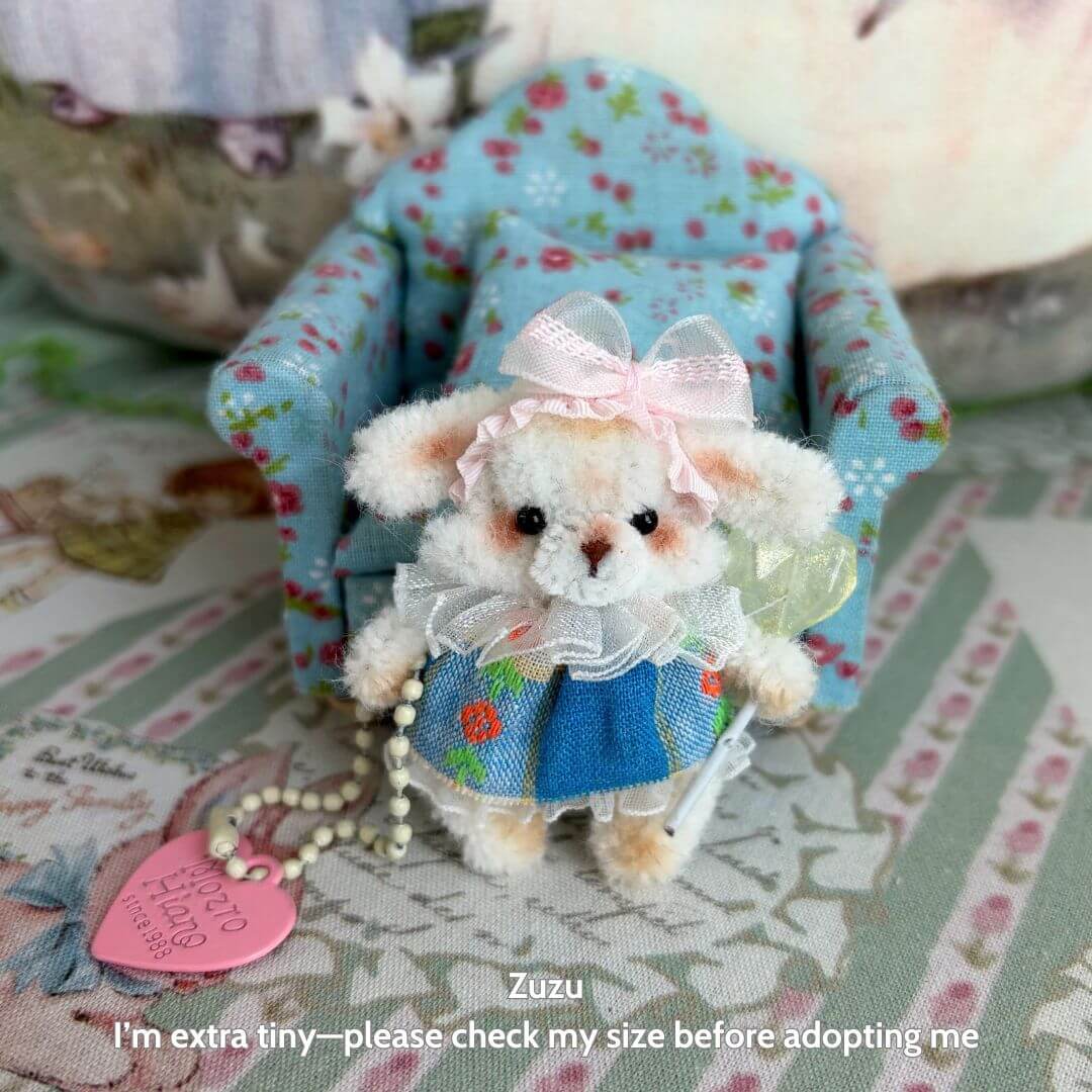 Miniature Pipe Cleaner Animals: handmade kitten in blue dress with floral apron and pink bow, posing next to tiny chair.