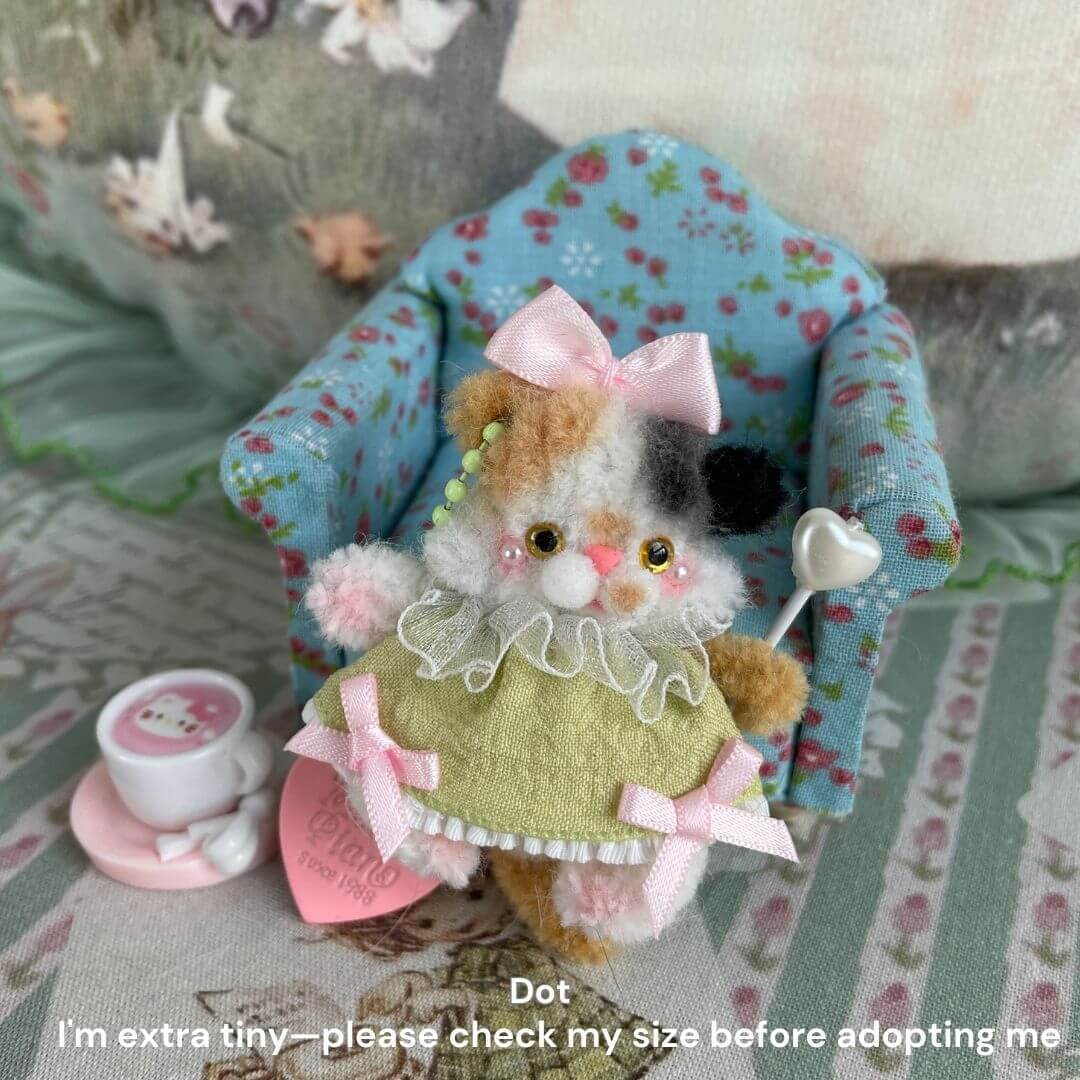 Handmade miniature pipe cleaner puppy with green dress and pink bow, sitting on floral chair with teacup accessory.