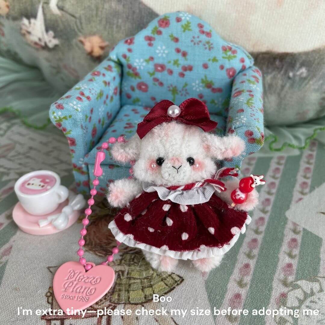 Miniature plush sheep toy in red polka dot dress on dollhouse chair, holding tiny heart-shaped accessory, perfect for decor.