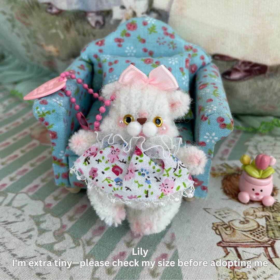 Handmade pipe cleaner animal keychain with bow, flower dress and pink beads, sitting in a floral armchair.