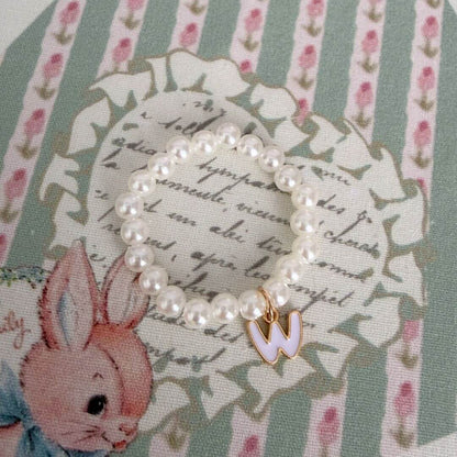 Initial Pearl Necklace with faux pearls and a delicate gold letter charm on a floral background.