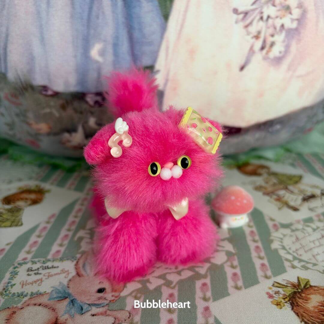Miniature pink fluffy kitten from the Glossy Meowgic Collection, adorned with decorations, whimsical and cute style.