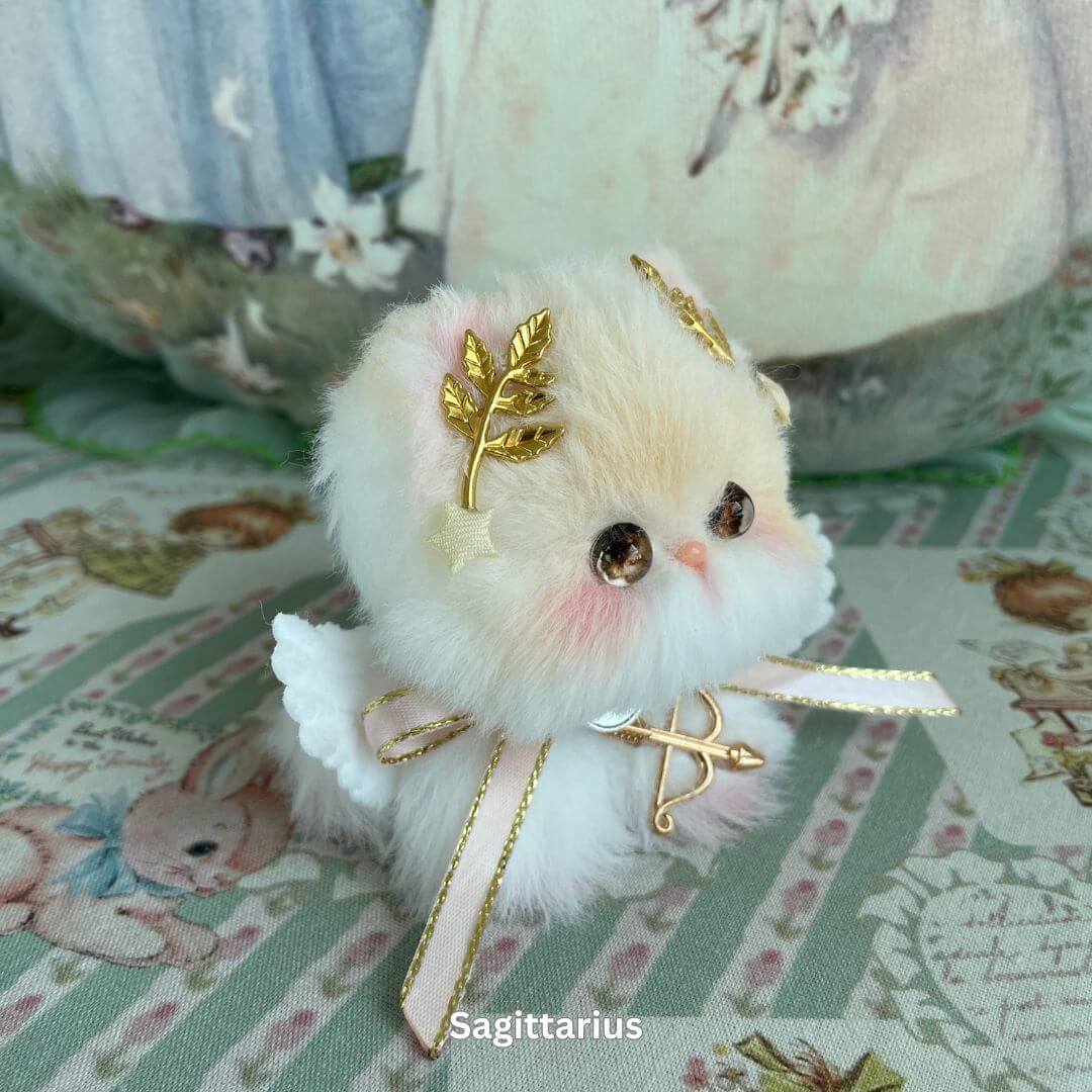 Sagittarius zodiac kitten plush toy with gold leaf accessories, faux fur, and a bow on a patterned fabric, from the Zodiac Kitten Collection.