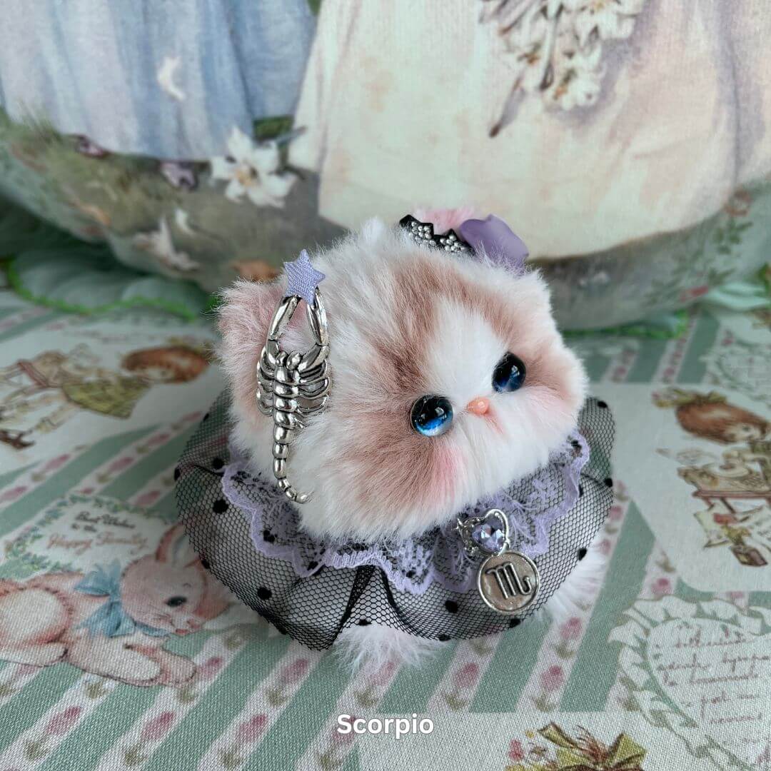 Scorpio inspired plush kitten with decorative charm, faux fur, and violet ribbon from the Zodiac Kitten Collection on floral background.