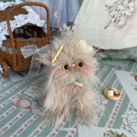 Handmade long-haired plush kitten toy with fluffy fur and bow, from Siberian Snuggles Collection, next to a miniature wicker carriage.