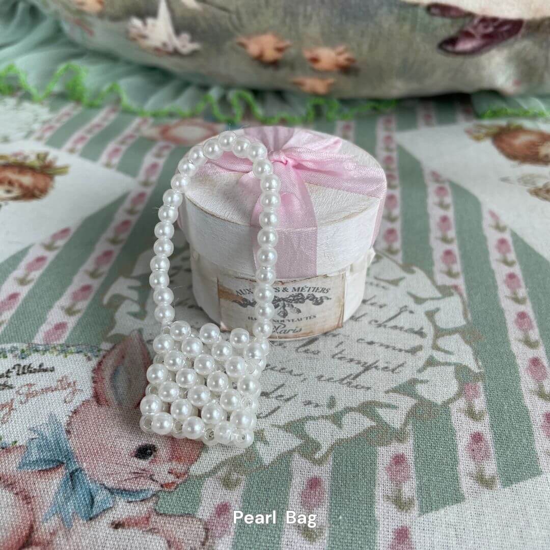 White pearl mini bag for plush toys, ideal as a stylish accessory for kittens or puppies, placed on a decorative floral background.