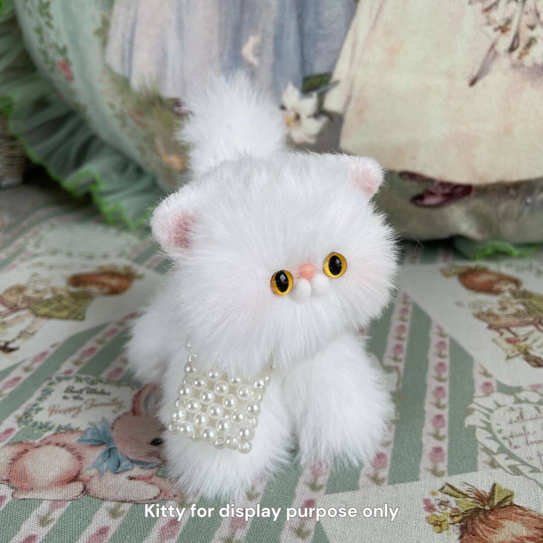 Handmade fluffy plush kitten with a pearl accessory on embroidered fabric background.