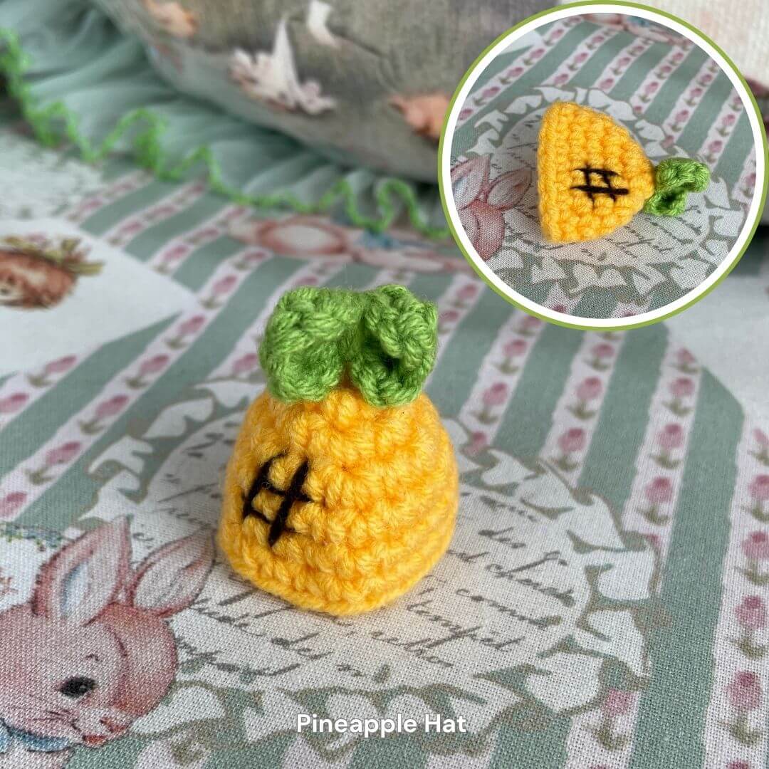 Handmade pineapple hat accessory for plush toys or small pets, featuring a cute yellow and green crochet design on a patterned fabric backdrop.