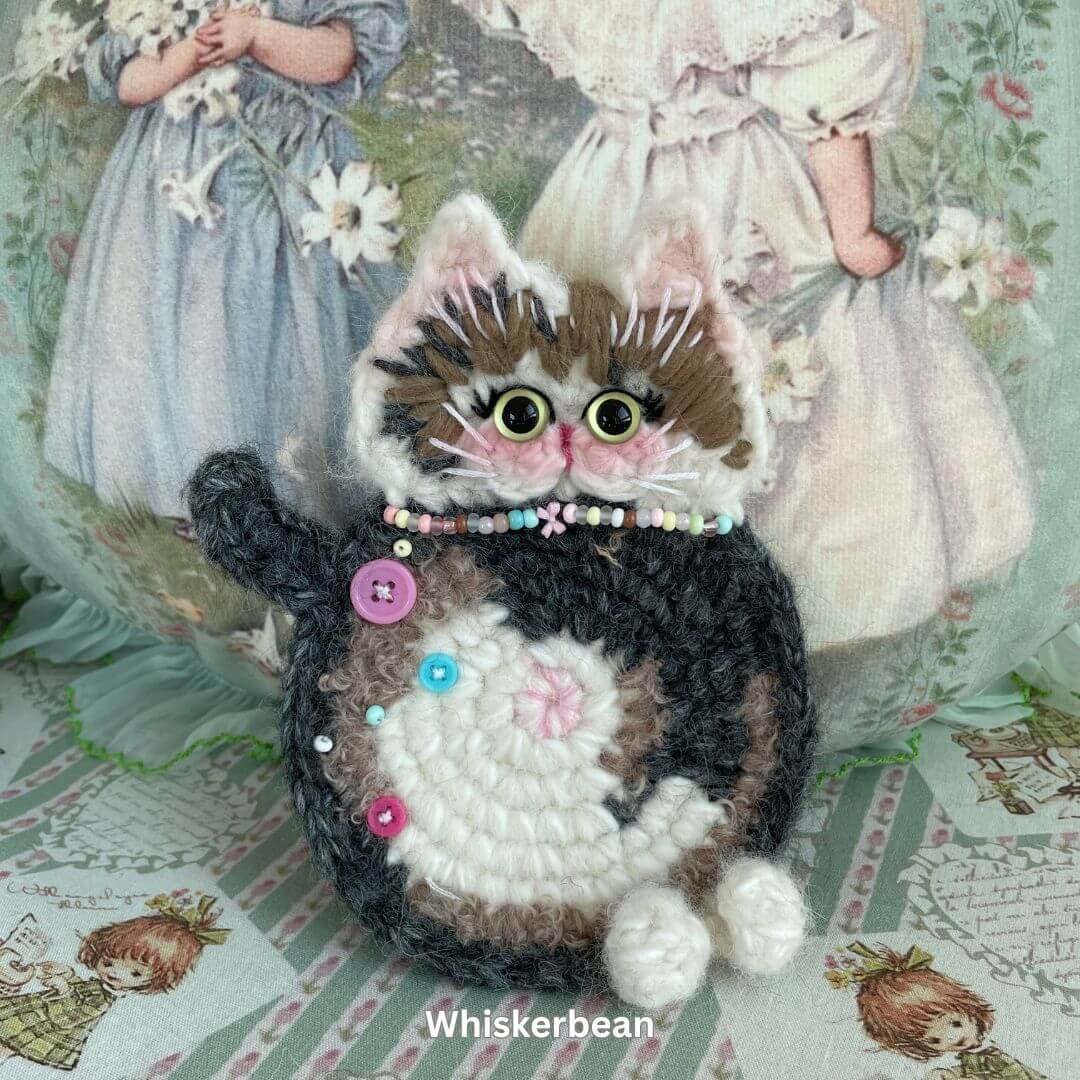Handmade cat-themed plush accessory by SnugglePaws, featuring a cute kitten design with colorful beads, buttons, and stitching details.