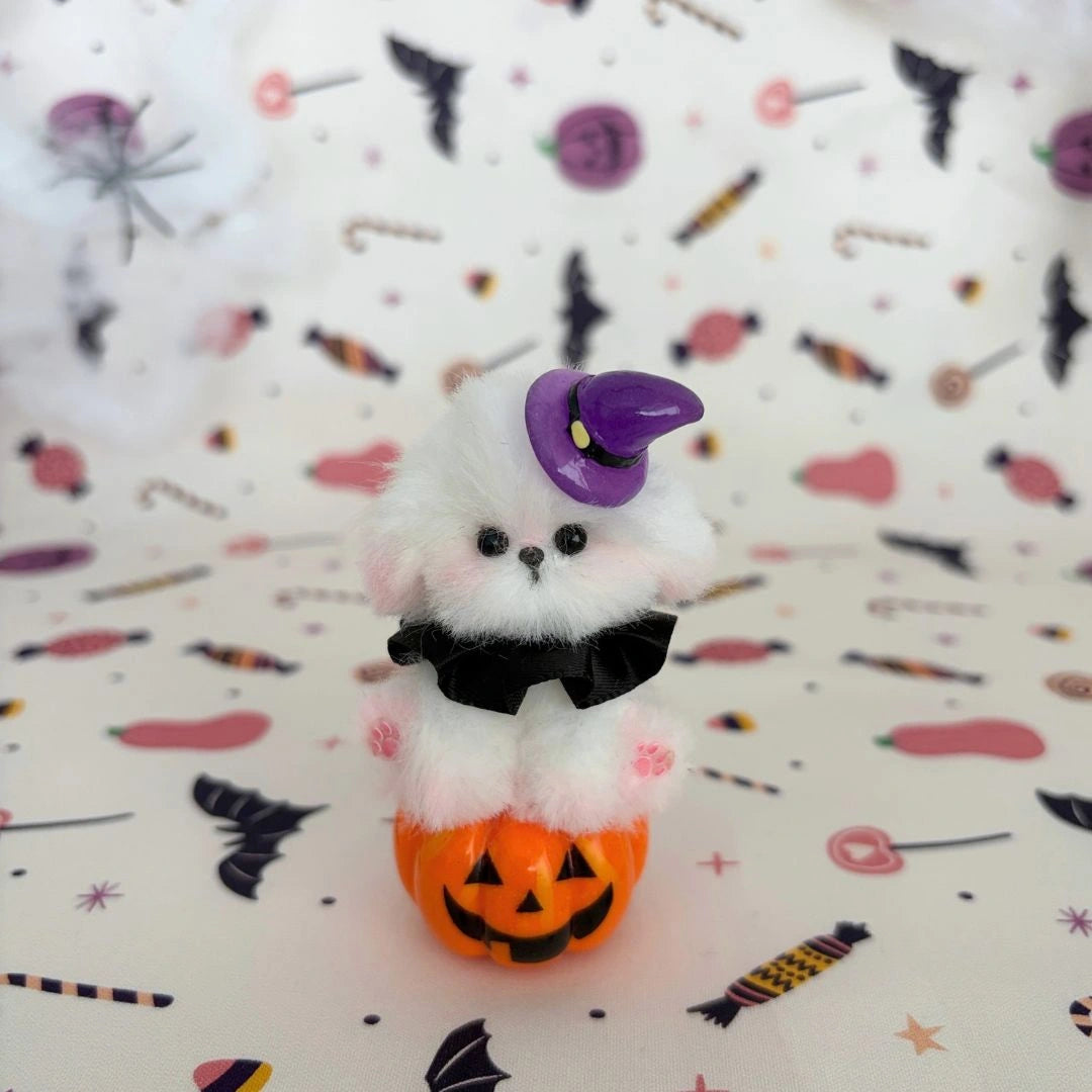 White fluffy friend on a pumpkin with a purple witch hat and black bow.
