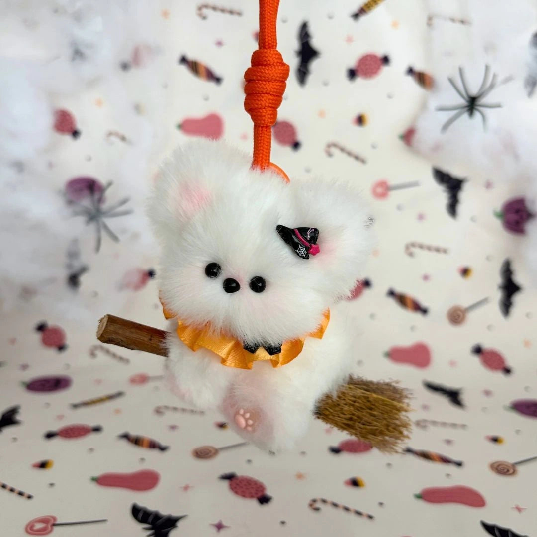 White fluffy friend on a broom with an orange ruff and tiny witch-hat charm.