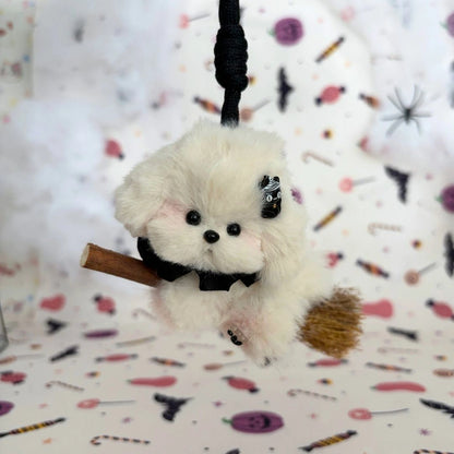 Cream floppy-eared friend riding a broom with a black ruff and tiny mummy charm.