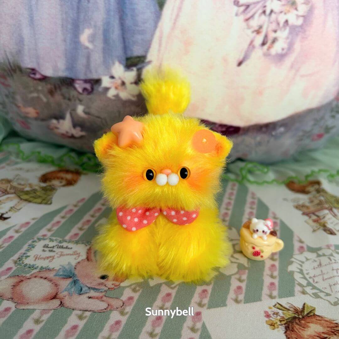 Glossy Meowgic Collection - fluffy yellow handmade kitten with a star accessory, polka dot bow, next to a tiny cat figurine.