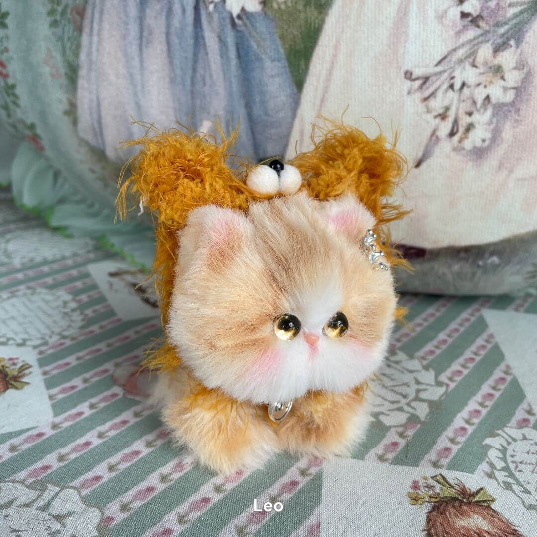 Handmade Leo plush kitten from Zodiac Collection, featuring lion-like mane and jewelry, on a patterned background.